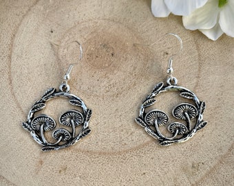 May include: Silver earrings with a circular design featuring three mushrooms and leafy branches.
