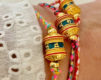 Bracciale in corda intrecciata con ruota di preghiera buddista tibetana placcata in oro 18k/blu con iscrizione "Om Mani Padme Hum" su una scelta di corda colorata