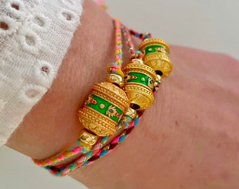 Bracciale in corda intrecciata con ruota di preghiera buddista tibetana placcata in oro 18k con iscrizione "Om Mani Padme Hum" su un cordino di colore a scelta.