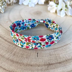 Peut inclure: Un bracelet en tissu blanc avec un motif floral dans les tons bleus, rouges et verts. Le bracelet est double et possède un fermoir argenté.