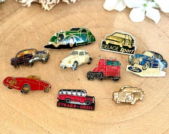 May include: A collection of vintage car enamel pins, including a red truck, a white Volkswagen Beetle, a green Delage Sport car, a blue Ford, and a red bus. The pins are all in excellent condition and would make a great addition to any car enthusiast's collection.