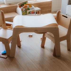 May include: A wooden table and two chairs, perfect for a child's play area. The table has a white paper roll on top, and the chairs are made of light wood.