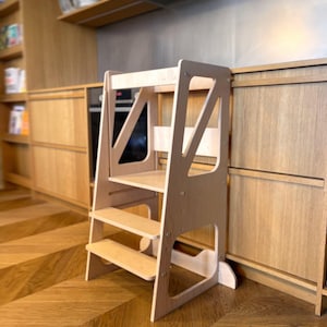 Può includere: Uno sgabello in legno chiaro a tre gradini con una barra di sicurezza. Il design è semplice e funzionale, ideale per aiutare i bambini a raggiungere piani di lavoro o altre superfici rialzate in una cucina o ambiente simile.