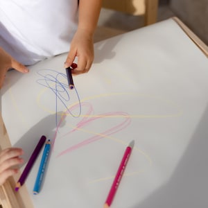 May include: Two children are drawing on a white surface with colorful pencils. The pencils are arranged on the table, and the children are using them to create lines and shapes.