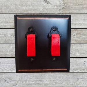 May include: A black electrical outlet cover with two red toggle switches.