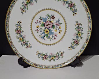 May include: A white porcelain plate with a floral design. The plate features a central floral bouquet and smaller floral arrangements around the rim. The rim is trimmed with a gold border and a delicate floral pattern.