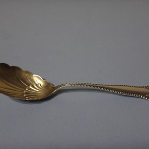 Puede incluir: Una cuchara de azúcar de plata con un cuenco festoneado y un mango con cuentas. El mango tiene un diseño floral en el extremo.