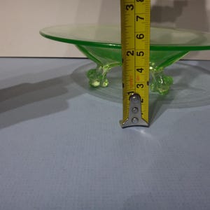 May include: A green glass pedestal dish with three feet. The dish is 7.6 cm tall.