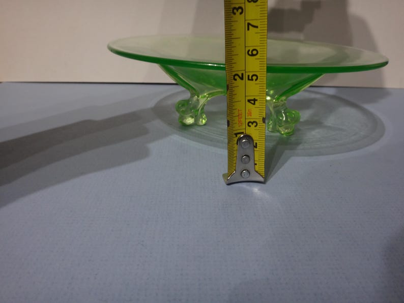 May include: A green glass pedestal dish with three feet. The dish is 7.6 cm tall.