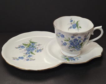 May include: A white teacup and saucer set with a floral design. The teacup and saucer are white with a gold trim and a blue floral pattern. The set includes a teacup, a saucer, and a serving plate.