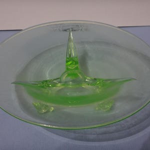 May include: A green glass bowl with three legs and a pointed centre piece. The bowl is clear and has a frosted finish.