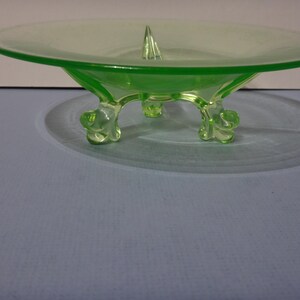 May include: A green glass footed bowl with a raised centre point. The bowl has three legs that are shaped like stylised animal paws.