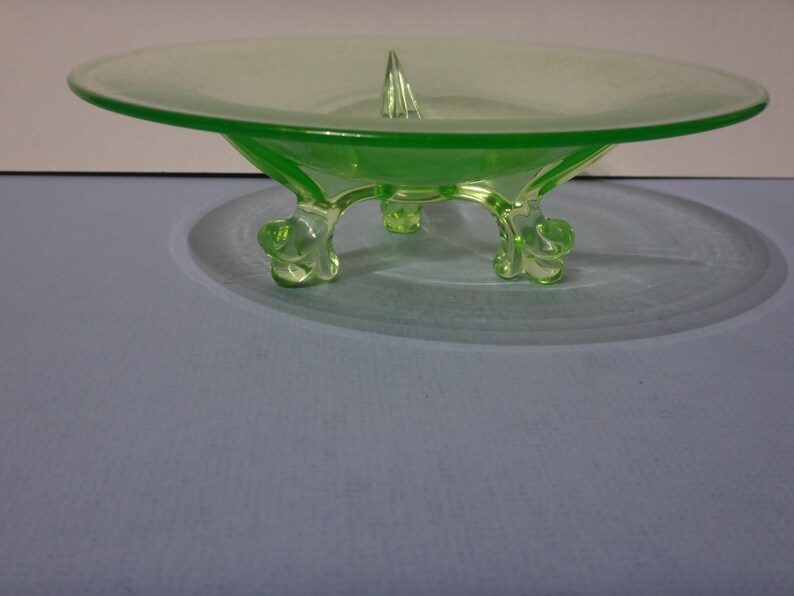 May include: A green glass footed bowl with a raised centre point. The bowl has three legs that are shaped like stylised animal paws.