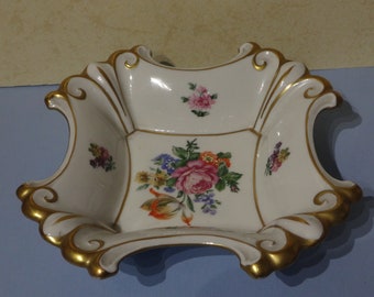 Puede incluir: Un tazón de porcelana blanca con un borde festoneado y ribete dorado. El tazón está decorado con diseños florales en tonos de rosa, rojo, amarillo y azul.