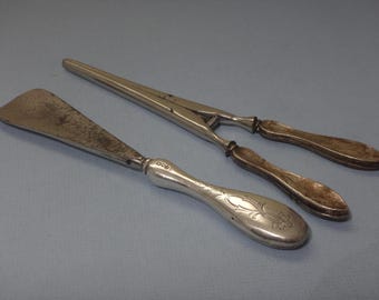 May include: A set of two antique silver shoe horns. One horn has a decorative handle with an engraved floral design. The other horn is a pair of silver shoehorn tongs.