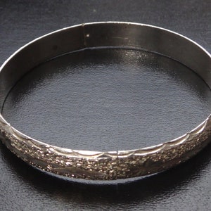 May include: A silver bangle bracelet with a textured design.