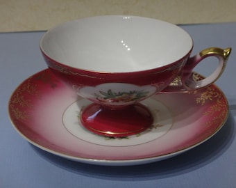 May include: A pink and white teacup and saucer set with gold trim and floral designs. The cup has a handle and a pedestal base.