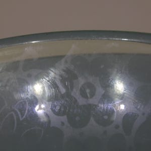 May include: A close-up of a grey glass bowl with a frosted design. The bowl has a smooth, rounded rim and a slightly textured surface.