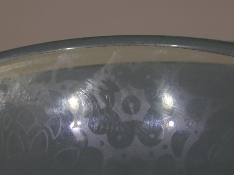 May include: A close-up of a grey glass bowl with a frosted design. The bowl has a smooth, rounded rim and a slightly textured surface.