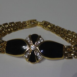 May include: A gold chain bracelet with a black enamel and rhinestone flower design.