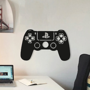 Puede incluir: Un escritorio blanco con un portátil, un cuaderno y una lámpara negra. Un mando de PlayStation negro está montado en la pared. Hay dos cuadros enmarcados en la pared detrás del escritorio.