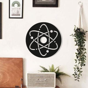 Peut inclure: Décoration murale en forme de symbole d'atome noir et blanc. L'art mural rond présente un motif découpé de la structure d'un atome. L'atome est monté sur un mur blanc, entouré d'œuvres encadrées, d'un tourne-disque et d'un haut-parleur.
