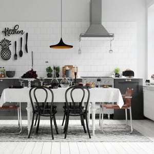 Può includere: Scena di cucina moderna con un tavolo da pranzo apparecchiato. Il tavolo è coperto da una tovaglia bianca e circondato da sedie nere. Un ananas decorativo e la parola "Kitchen" sono sul muro.