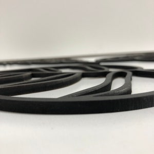 以下が含まれることがあります： 黒色のレーザーカット装飾品。葉のようなデザインで、マットな仕上がり。白い背景に配置され、曲線と丸みを帯びたエッジが特徴です。