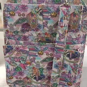 May include: A multi-pocket backpack with a colorful pattern featuring castles, books, and floral designs. The bag has a detachable strap and silver-tone hardware. The color palette includes pink, purple, and green.