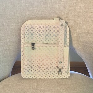 May include: A pastel-colored crossbody bag with a repeating pattern of hearts and Mickey Mouse silhouettes. The bag features a zippered pocket, a small pocket, and a silver-tone clasp. The bag is made of a soft, fabric material.