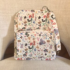 May include: A white crossbody bag with a colorful pattern featuring Disney characters and icons. The bag has a zippered front pocket, multiple compartments, and a detachable strap. The pattern includes images of Ariel, Mickey Mouse, and Cinderella's castle.