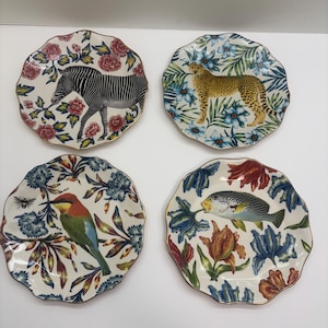 Puede incluir: Juego de cuatro platos decorativos con bordes festoneados y bordes dorados. Cada plato presenta un animal o criatura diferente: una cebra, un guepardo, un p&aacute;jaro y un pez, rodeados de dise&ntilde;os florales.