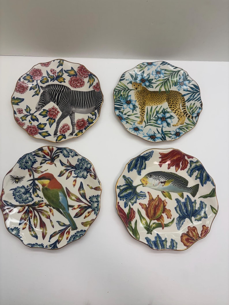 Puede incluir: Juego de cuatro platos decorativos con bordes festoneados y bordes dorados. Cada plato presenta un animal o criatura diferente: una cebra, un guepardo, un p&aacute;jaro y un pez, rodeados de dise&ntilde;os florales.