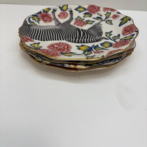 Puede incluir: Una pila de cuatro platos decorativos. Cada plato presenta un dise&ntilde;o de cebra en blanco y negro, rodeado de flores rojas, hojas verdes y un borde dorado. Los platos tienen un borde festoneado.
