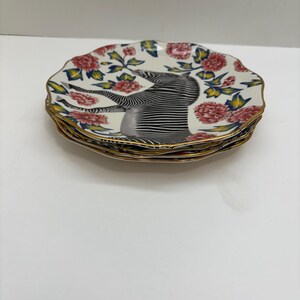 Puede incluir: Una pila de platos decorativos con un dise&ntilde;o floral y de cebra. Los platos tienen un fondo blanco con flores rojas y rosas, hojas verdes y un borde dorado. El centro de cada plato presenta una ilustraci&oacute;n de cebra.