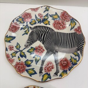 Puede incluir: Un plato decorativo con dise&ntilde;o de cebra. El plato presenta un fondo blanco con una ilustraci&oacute;n de cebra en blanco y negro. Est&aacute; adornado con patrones florales rojos y rosas y un borde dorado. El plato tiene un borde festoneado.