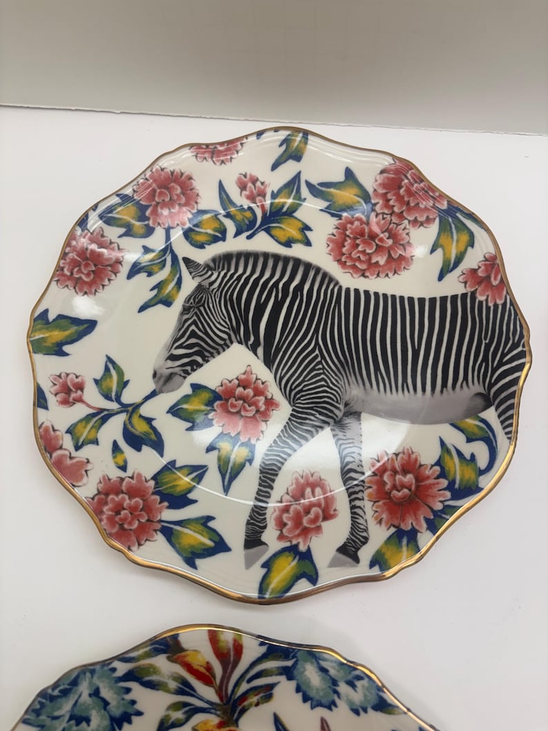 Puede incluir: Un plato decorativo con dise&ntilde;o de cebra. El plato presenta un fondo blanco con una ilustraci&oacute;n de cebra en blanco y negro. Est&aacute; adornado con patrones florales rojos y rosas y un borde dorado. El plato tiene un borde festoneado.