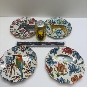 Puede incluir: Cuatro platos decorativos de cer&aacute;mica con bordes festoneados. Cada plato presenta un dise&ntilde;o diferente de animal o vida acu&aacute;tica: una cebra, un leopardo, un p&aacute;jaro y un pez. Los platos tienen un borde floral y un ribete dorado.