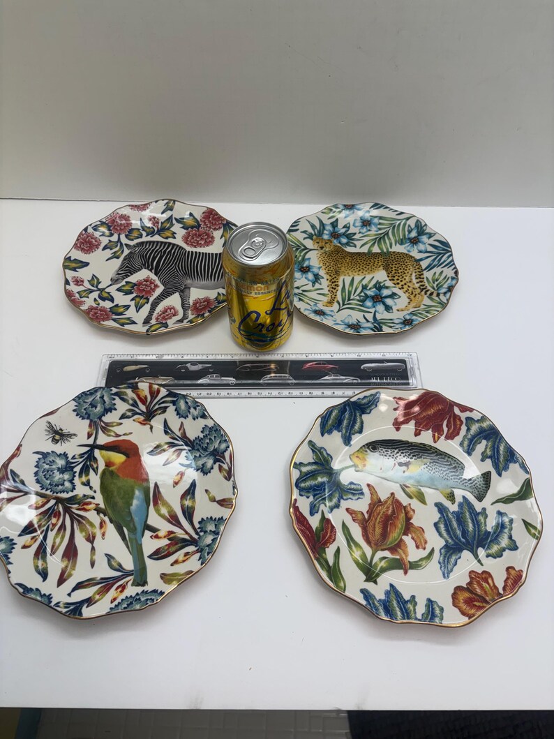 Puede incluir: Cuatro platos decorativos de cer&aacute;mica con bordes festoneados. Cada plato presenta un dise&ntilde;o diferente de animal o vida acu&aacute;tica: una cebra, un leopardo, un p&aacute;jaro y un pez. Los platos tienen un borde floral y un ribete dorado.