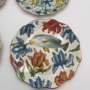 Puede incluir: Una colecci&oacute;n de platos decorativos con bordes dorados. Un plato presenta un dise&ntilde;o de leopardo con detalles florales azules. Otro plato muestra un pez rodeado de patrones florales rojos, azules y naranjas. Los platos tienen un borde festoneado.