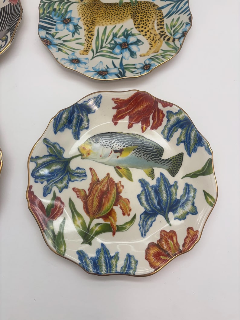Puede incluir: Una colecci&oacute;n de platos decorativos con bordes dorados. Un plato presenta un dise&ntilde;o de leopardo con detalles florales azules. Otro plato muestra un pez rodeado de patrones florales rojos, azules y naranjas. Los platos tienen un borde festoneado.