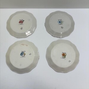 Puede incluir: Cuatro platos de cer&aacute;mica blanquecina con bordes festoneados. Cada plato presenta un dise&ntilde;o floral diferente en el centro, con el texto "Nature's Table" y "Jim Eder". Los platos est&aacute;n dispuestos sobre una superficie blanca.