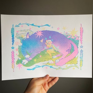 Peut inclure: Un chat rose et bleu pastel avec une fée assise sur son dos. Le chat dort dans un champ de fleurs et d'étoiles. La fée a des ailes et une baguette magique. L'image est entourée d'une bordure de feuilles et de fleurs.