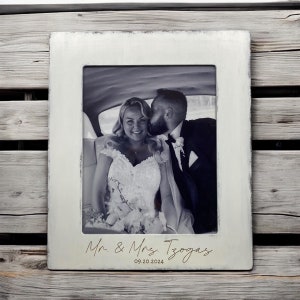 Peut inclure: Cadre photo rectangulaire blanc avec une finition vieillie. Il contient une photo en noir et blanc d'un couple. Le texte "Mr. & Mrs. Tzogas" et la date "09.20.2024" sont en bas du cadre.
