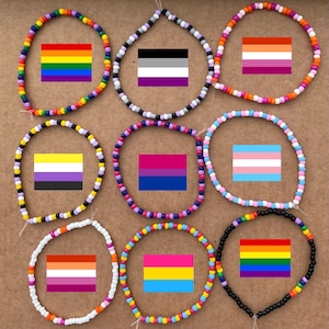 Puede incluir: Nueve pulseras de cuentas con diferentes banderas del orgullo. Las pulseras están hechas con cuentas de colores y presentan las banderas del arcoíris, transgénero, bisexual, lesbiana, genderqueer, pansexual, asexual y no binario.
