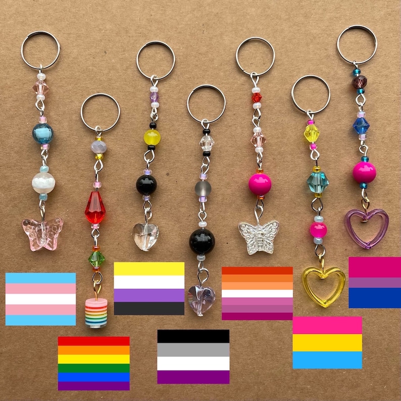 May include: Seven colorful beaded keychains with different charms, including butterflies, hearts, and crystals. Each keychain is paired with a different pride flag, representing various LGBTQ+ identities.