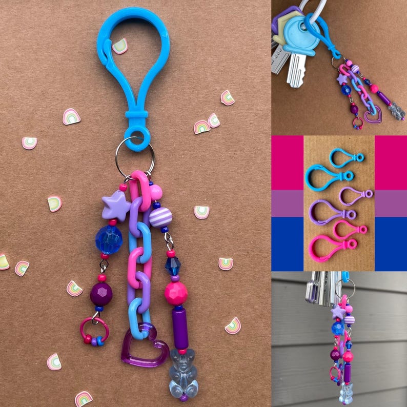 Op de afbeelding: Een blauwe sleutelhangerclip met een kralenbedel. De bedel bevat een paarse ster, blauwe en roze kralen, een hart en een gummybeer. Extra sleutelhangers en sleutelhangers met sleutels zijn ook afgebeeld.