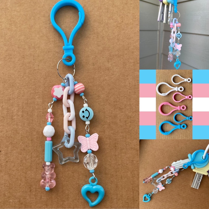 Op de afbeelding: Een blauwe sleutelhanger met een karabijnhaak, versierd met een ketting, kralen en bedels. De bedels zijn onder meer een gummybeer, een ster, een vlinder, een smiley en een hart. Het kleurenpalet is pastelroze, blauw en wit.