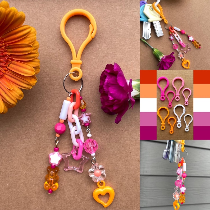 Op de afbeelding: Een sleutelhanger met een gele clip, versierd met roze, witte en oranje kralen, sterren en een hartvormige bedel. De sleutelhanger heeft ook een kleine gummybeer bedel. Andere sleutelhangers en clips zijn afgebeeld.