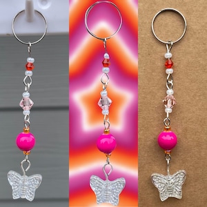 May include: A pink and clear butterfly charm keychain with a silver ring, pink beads, and clear crystal beads.